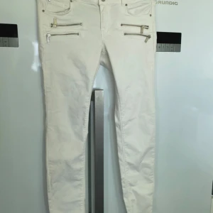 Vita byxor med dragkedjor - Ett par vita byxor med flera dragkedjor som detaljer. Byxorna har en smal passform och är midwaist.