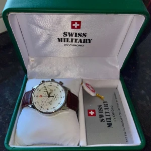 Swiss Military Designer Klocka - Swiss Military by Chromo klocka (Eta g15.211). Brunt läder. Nypris ca 3200 kr.  Nyskick, present från jobbet.  Box, instruktioner och äkthetsbevis ingår. Batteriet är trasigt men går att reparera. Därav priset.