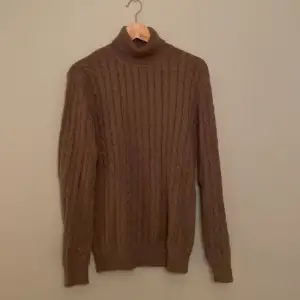 En grå/brun (taupe) polo/turtleneck tröja  från varumärket John Henric. 100% bomull  Kabelstickad  Tröjan är i mycket gott skick (9/10)