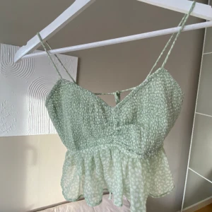 Topp - Supersöt grön topp från Gina Tricot! Ett somrigt linne med vitt mönster och knytning i ryggen. Något kortare i modellen med en volang nertill. Storleken går att justera med knytningen 