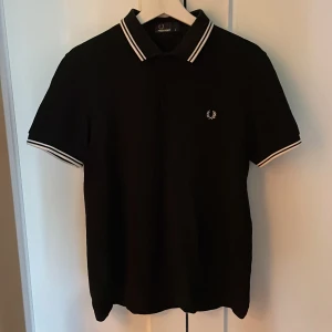 Fred Perry piké - Svart Fred Perry piké med vita detaljer. Tröjan är i mycket bra skick. Nypris ligger på 1 000 kr.