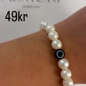 Pärlarmband med svart detalj - Ett elegant pärlarmband med vita pärlor och en svart detalj. Perfekt för både vardag och fest.