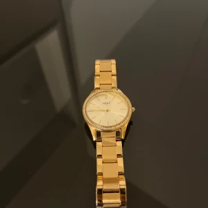Klocka - Snygg damklocka i guld med strass. Klockan är i bra skick och fungerar som den ska. Den har ett kvartsurverk och en guldpläterad armband.