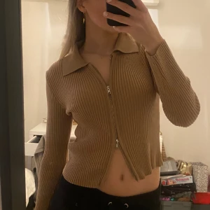 Brun tunn stickad ribbad tröja med dragkedja - Brun/beige tunnt stickad och ribbad tröja! Pikékrage Silvrig dragkedja som kan dras både uppifrån och nerifrån. Stl xs men passar även s Väldigt bra skick och väldigt mjukt och skönt material🤎🤎