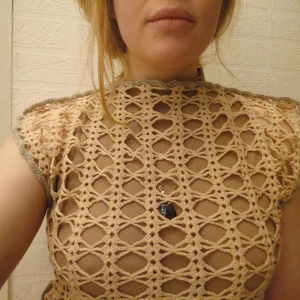 Virkad väst eller t-shirt / topp i beige och grå - En snygg virkad topp eller väst som går att bära över t.ex. en tröja med längre ärmar. Beige med x-mönster, grå stygn på sidor och vid hals och ärmar.