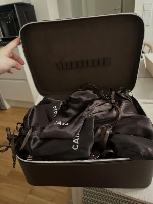Brun sminkväska från CAIA - Rymlig svart sminkväska från CAIA med satin påsarna inuti. Väskan har dragkedja och elastiska band på insidan av locket för att hålla sminkborstar eller verktyg på plats. Perfekt för att organisera dina skönhetsprodukter. Den är från senaste julkalendern och är aldrig använd, kommer att fraktas med lådan som den kom i🥰