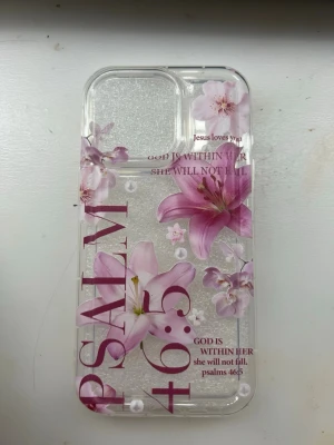 Blommigt mobilskal till iPhone 13 Pro - Snyggt genomskinligt mobilskal med rosa liljor och texten 'PSALM 46:5' samt citat på engelska. Skalets material är plast. Passar iPhone 13 Pro.