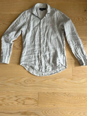 Ljusgrå linneskjorta Polo Ralph Lauren - Snygg ljusgrå skjorta i linne från Polo Ralph Lauren. Slim fit-modell med klassisk krage, storlek M