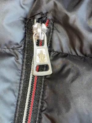 Svart dunjacka från Moncler - Snygg svart dunjacka från Moncler med glansigt yttertyg och detaljerad dragkedja med Moncler-logga. Jackan har klassisk quiltad design och är perfekt för kalla vinterdagar. Passar dig som vill ha både stil och värme.