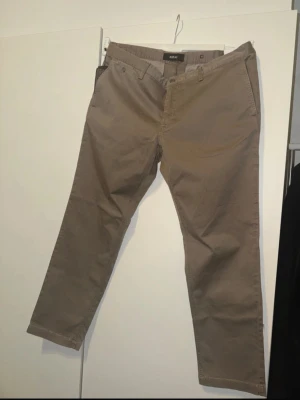 Byxor replay  - Snygga beiga chinos från replay med klassisk rak passform. Byxorna har sidofickor, bälteshällor och två bakfickor med knapp. Tillverkade i mjukt bomullstyg som ger en skön känsla och stilren look.