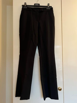 Svarta kostymbyxor från Zara - Stilrena svarta kostymbyxor från Zara med låg midja och pressveck. Byxorna har en klassisk midja och är tillverkade i ett slätt tyg som ger en elegant look. Perfekta för dig som vill ha en clean och tidlös stil.