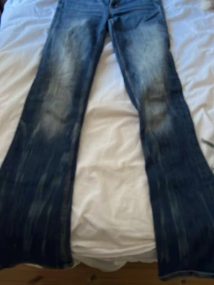 Blå bootcut jeans  - Säljer ett par blå bootcut jeans från weekday. Jeansen har en klassisk femficksmodell och en grön Replay-lapp bak i midjan. Materialet är denim i bomull och passformen är utsvängd nedtill.