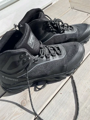 Svarta vattentäta kängor från Everest stl 40 - Säljer ett par svarta kängor från Everest med högt skaft och snörning. Kängorna är tillverkade i slitstarkt syntetmaterial och har vattentätt membran. Snygg sportig design med reflexdetaljer och robust sula som passar perfekt för utomhusaktiviteter. Stl 40