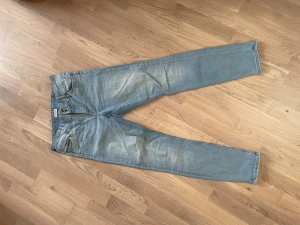 Ljusblå skinny jeans från Lindex - Säljer ett par ljusblå skinny jeans från Lindex med slitningar och tvättade detaljer. Jeansen har två knappar i midjan, dragkedja på fickan och klassisk femficksmodell. Perfekta för en avslappnad och trendig look.