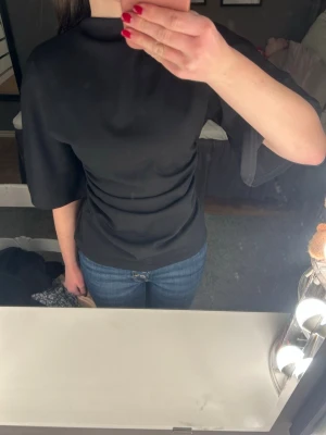 Svart topp - Svart halvpolo med trekvartsärm och vida ärmar. Resår i midjan.