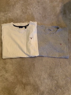2-pack GANT t-shirts vit & grå - Säljer två klassiska t-shirts från GANT, en i vitt och en i ljusgrått. Båda har rund hals, korta ärmar och liten broderad logga på bröstet. Perfekta basplagg i mjuk bomull som funkar till allt. Storlek 158