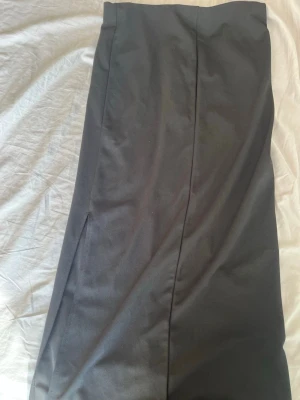 Svart långkjol med slits - Klassisk svart långkjol med rak passform och diskret slits på sidan. Kjolen har en stilren look och passar perfekt till många olika outfits. Tillverkad i ett mjukt och följsamt material som ger en snygg siluett.