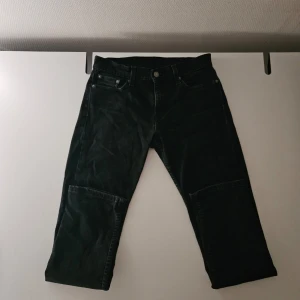 Svarta raka jeans från Levi's - Säljer ett par svarta jeans från Levi's med raka ben och klassisk femficksdesign. Jeansen har synliga sömmar och patchdetaljer vid knäna för en cool look. Tillverkade i denim med en något tvättad finish. Perfekta för en avslappnad streetstil.