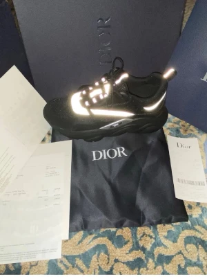 Svarta D!or sneakers med reflexdetaljer - Säljer ett par svarta D!or sneakers med feta sulor och reflekterande detaljer. Skorna har en chunky design, snörning och är tillverkade i en mix av läder och textil. Perfekta för dig som vill sticka ut med exklusiva och trendiga sneakers.