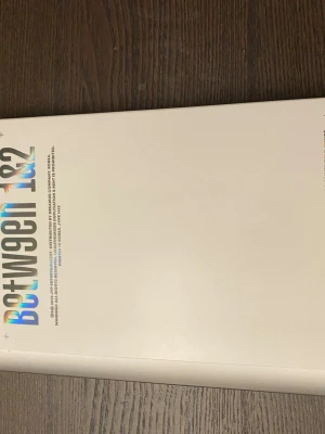 Between 1&2 vit album  - Säljer en stilren vit bok med titeln 'Between 1&2' i holografisk text på omslaget. Boken har en modern design och hårda pärmar. Perfekt för dig som gillar snygga och unika böcker i bokhyllan. K-POP