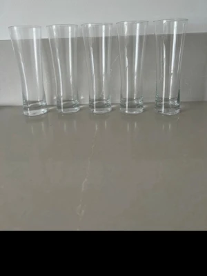 Fem höga dricksglas i glas - Säljer fem stycken höga, genomskinliga dricksglas med smalare midja och bredare öppning. Perfekta för kalla drycker och snygga att ha framme på bordet. Tillverkade i klart glas och har en stilren, enkel design.