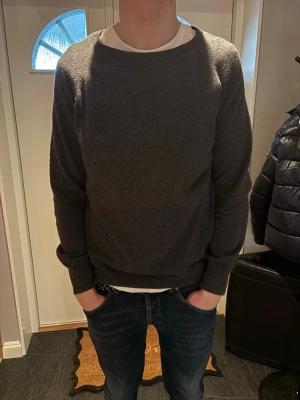 Stickad tröja från Oscar Jacobsson  - En enkel och stilren mörkgrå tröja med rund halsringning och långa ärmar. Tröjan har ribbade muddar vid ärmslut och nederkant, och är tillverkad i en mjuk ullblandning. Perfekt för lager på lager och passar till det mesta. Skriv vid frågor. Priset kan diskuteras.