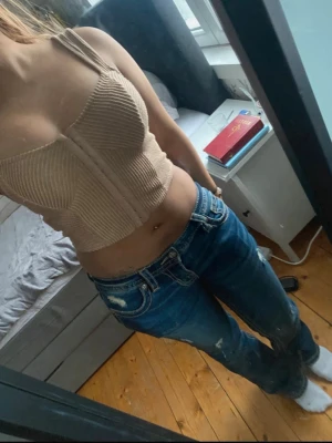 Beige ribbad croppad topp Forever 21 - Säljer en beige croppad topp från Forever 21 med ribbad struktur och breda axelband. Toppen har en snygg, figurnära passform och markerad söm framtill. Perfekt till jeans eller kjol för en trendig look.