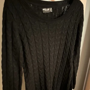 Svart kabelstickad tröja  - Säljer en svart kabelstickad tröja med rund halsringning och långa ärmar. Tröjan har ett klassiskt flätmönster och ribbade muddar vid hals, ärmslut och nederkant. Perfekt för dig som gillar enkel och stilren design.