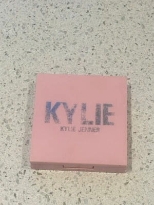 Kylie Jenner bronzer Tanned and Gorgeous - Säljer ett pressat bronzingpuder från Kylie Jenner i färgen 400 Tanned and Gorgeous. Kommer i en snygg rosa fyrkantig dosa med spegel. Perfekt för att ge ansiktet en solkysst look och definiera kindbenen.