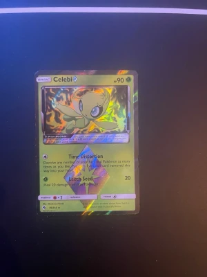 Pokémonkort Celebi Prism Holo - Säljer ett samlarkort från Pokémon, Celebi Prism Holo. Kortet har en glansig holografisk yta med gröna och gula färger och motivet av Celebi. Kortet har 90 HP och attacker som Time Distortion och Leech Seed. Perfekt för samlare eller Pokémonfans.