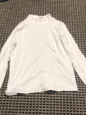 Vit polotröja med ribbad krage - Klassisk vit långärmad polotröja med ribbad hög krage. Tröjan är enkel och stilren, perfekt att matcha med olika outfits. Tillverkad i mjukt material som känns skönt mot huden. Passar dig som gillar minimalistisk stil.