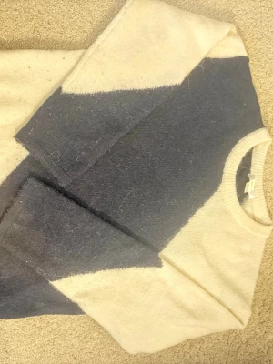 Stickad tröja från Gina Tricot - Säljer en snygg stickad tröja från Gina Tricot i beige och mörkblått. Tröjan har ett coolt färgblocksmönster, rund halsringning och långa ärmar. Perfekt för dig som gillar en avslappnad men trendig stil.