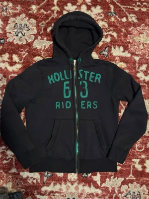 Svart Hollister zip hoodie - Hollister hoodie i fint skick!  Står storlek: L men den passar som S  Det har gjorts en lagning på dragkedjan då den hade släppt men nu fungerar den fint.  Mått:  Längd: ca 62cm Axelbredd: ca 42cm  Hör av dig vid funderingar! 