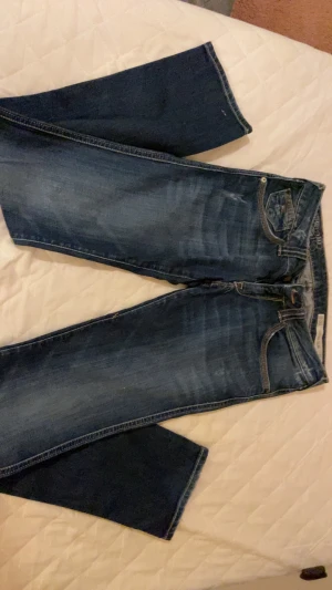 Mörkblå jeans från Levi's - Säljer ett par mörkblå jeans från Levi's med klassiska fem fickor och snygga slitningar framtill. Jeansen har en rak passform med något utsvängda ben och detaljerade sömmar på bakfickorna. Perfekta för en avslappnad och trendig look.