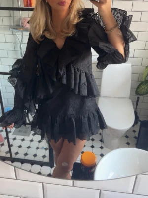 Svart volangklänning med spetsdetaljer - Supersnygg svart kortklänning med volanger och spetsdetaljer. Klänningen har v-ringning, långa ärmar med volang.