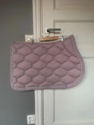 Ljuslila schabrak från PS of Sweden - Säljer ett ljuslila schabrak från PS of Sweden med quiltat mönster och dekorativ kant i silver och lila. Schabraket har en klassisk form och är tillverkat i ett mjukt, vadderat material som ger bra komfort till hästen. Perfekt för dig som vill ha en snygg detalj till din ridutrustning.storlek:full