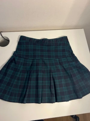 Grönrutig kortkjol från H&M aldrig använd - Snygg grön och svart rutig kortkjol från H&M med klassiskt rutmönster. Kjolen har en lätt utställd form och bred linning, perfekt för en trendig och avslappnad look. Tillverkad i mjukt och bekvämt material.