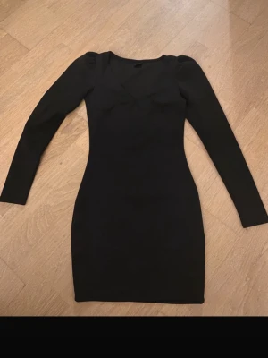 Svart långärmad kortklänning - Tajt svart klänning med lång ärm och v-ringning. Klänningen är kort och har en enkel, stilren design som framhäver figuren. Perfekt för dig som gillar minimalistisk stil och vill ha något klassiskt i garderoben. Från Gina Tricot 