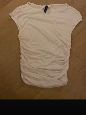 Vit ribbad topp från H&M - Säljer en enkel och snygg vit topp från H&M. Toppen är ribbad med rynkade sidor och har en ärmlös design med rund halsringning. Perfekt att matcha med jeans eller kjol för en clean look.