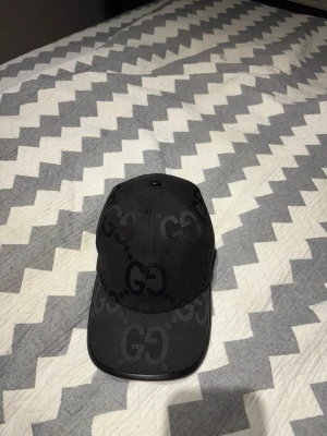 Svart keps från Gucci med GG-mönster - Snygg svart keps från Gucci med det klassiska GG-mönstret över hela kepsen. Kepsen har böjd skärm och är tillverkad i ett slitstarkt tygmaterial. Perfekt för dig som vill ha en stilren accessoar med lyxig känsla. Äkta 