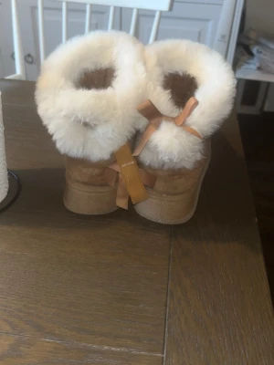 Bruna fluffiga skor med rosett - Fina skor med fluff och rosett, ena rosetten håller på att ramla av men går att fixa jätte lätt!