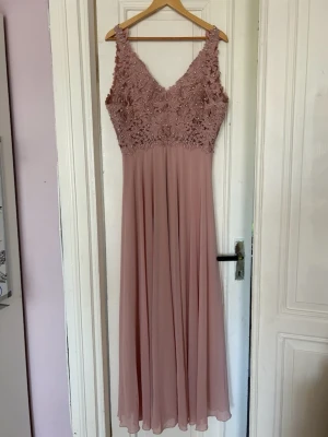 Lång rosa spetsklänning med v-ringning - Elegant långklänning i ljusrosa med v-ringad hals. Dragkedjan behövs tyvärr bytas ut så om du känner dig manad att göra det så är klänningen din!