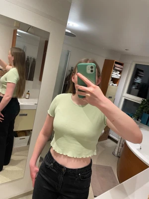 Ljusgrön croppad ribbad topp - Superfin ljusgrön croppad topp från Pull&Bear med ribbad struktur och korta ärmar. Toppen har vågig volangkant nertill och är perfekt för dig som gillar en trendig och avslappnad stil.