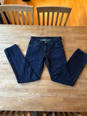 Mörkblå Lee jeans med rak passform - Snygga mörkblå jeans från Lee med klassisk rak passform och fem fickor. Jeansen har gylf med dragkedja och knapp, samt Lee-logga på både knapp och etikett. Perfekta för en stilren och tidlös look. Knappt andvända!