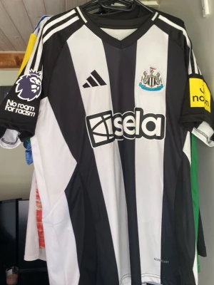 Newcastle United matchtröja Adidas - Snygg Newcastle United matchtröja från Adidas med svarta och vita ränder, klubbmärke på bröstet och Premier League-logga på ärmen. Tryck med 'Isak 14' på ryggen. Helt ny o aldrig använd✅