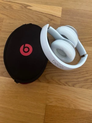 Vita Beats over-ear hörlurar - Snygga vita over-ear hörlurar från Beats med mjuka öronkuddar och justerbart huvudband. Kommer med ett svart fodral med röd Beats-logga. Perfekta för musik, gaming eller videos. Modern design i plast och konstläder. Är i fint skick, laddare finns ej men dem laddas med de gamla android laddarna.