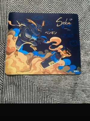 Soku gaming musmatta med penguin-motiv - Cool gaming musmatta från Soku med färgstarkt motiv av en tecknad penguin och japanska tecken. Musmattan är svart med inslag av blått, orange och beige, och har en mjuk yta som passar perfekt för gaming eller datorarbete.