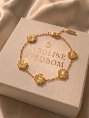 Guldigt blomarmband Caroline Svedbom - Säljer ett elegant armband från Caroline Svedbom i guldton med små blommor längs hela kedjan. Perfekt accessoar för dig som gillar detaljer och vill ha något unikt till din outfit. Lätt att matcha och ger en lyxig känsla.
