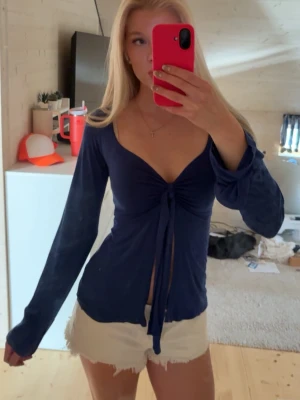 Mörkblå omlottopp med knyt - Trendig mörkblå omlottopp med långa ärmar och djup v-ringning. Toppen har snygg knytning framtill som ger en croppad känsla. Perfekt för dig som vill ha en stilren men ändå unik look.