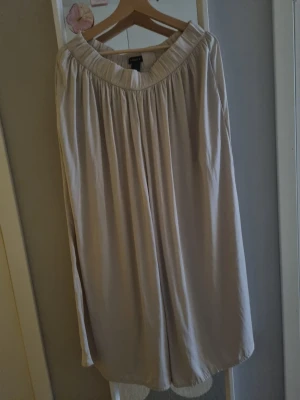 Beige lång kjol från Lindex - Luftiga och vida byxor från Lindex med resår i midjan. Byxorna har ett mjukt fall och är tillverkade i ett lätt tyg som ger en avslappnad känsla. 